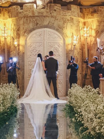 Brautpaar vor dem Altar in einem edlen Ballsaal mit verspiegeltem Weg von Blumen umrankt.