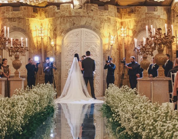 Brautpaar vor dem Altar in einem edlen Ballsaal mit verspiegeltem Weg von Blumen umrankt.