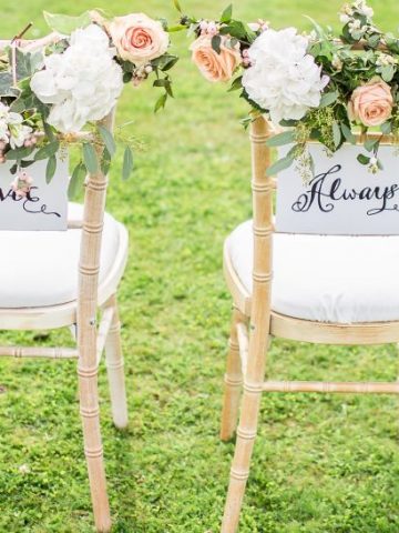 Mit Blumen dekorierte Stühle auf einer grünen WIese für das Brautpaar