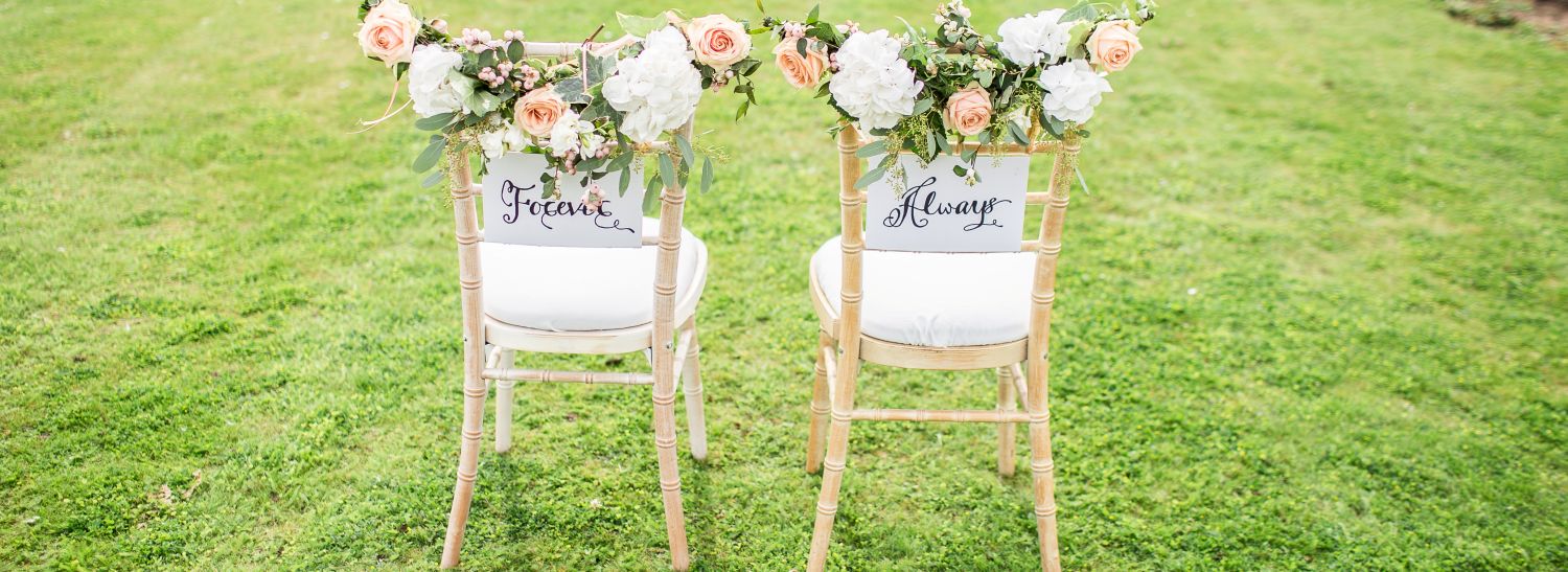 Mit Blumen dekorierte Stühle auf einer grünen WIese für das Brautpaar